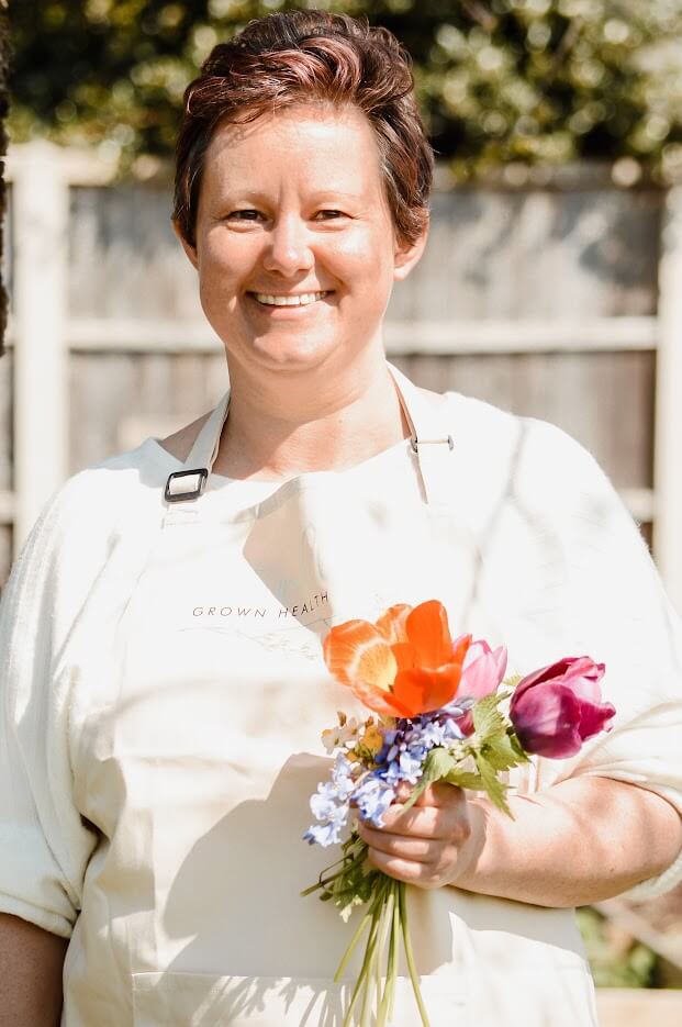 Amy standing holding flowers wearing a white top