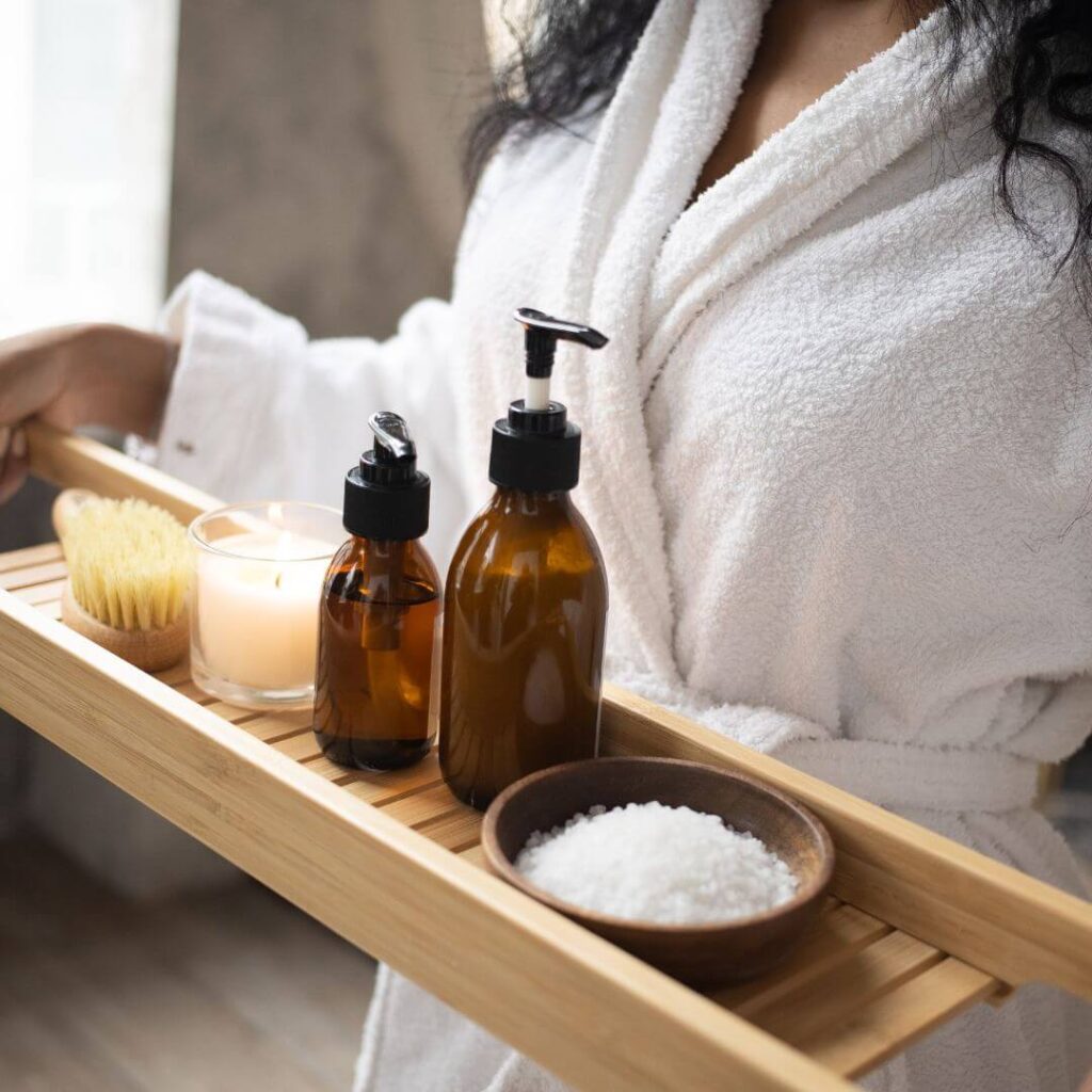Skincare products on a wooden board held by a lady in a white towelling robe